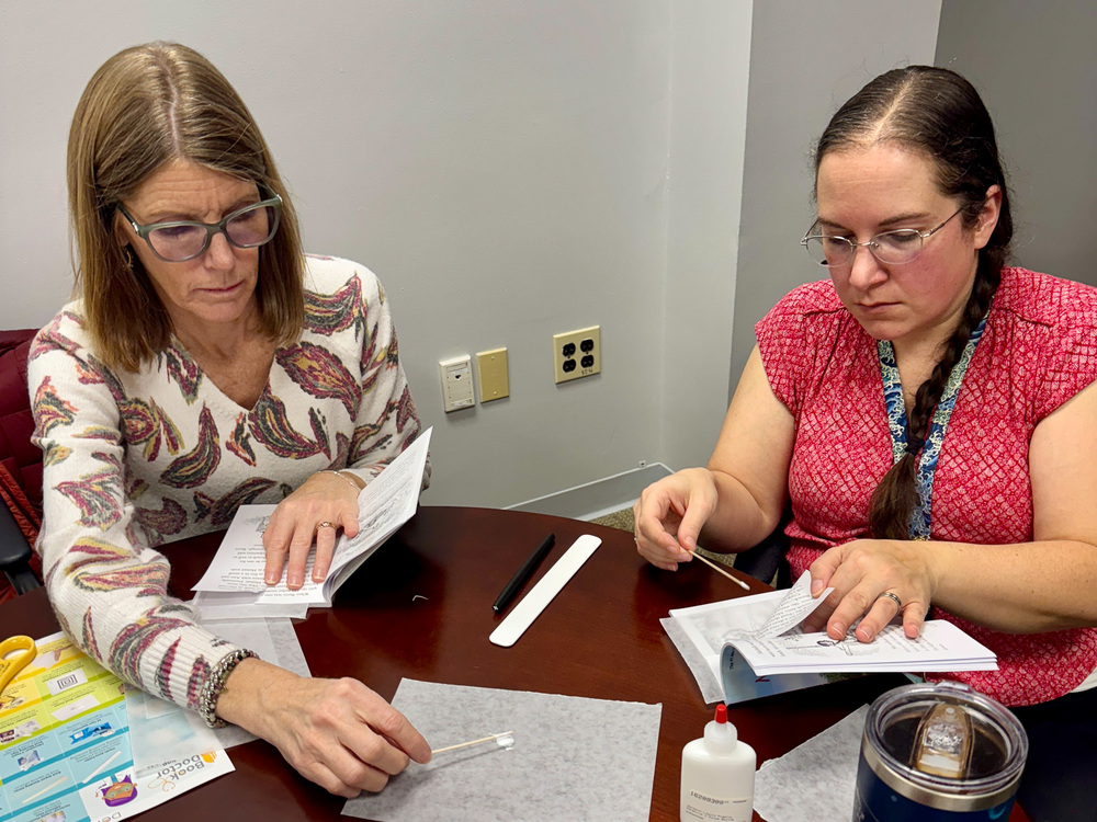 Two media center coordinators work with glue and cotton swabs to repair tears on book pages