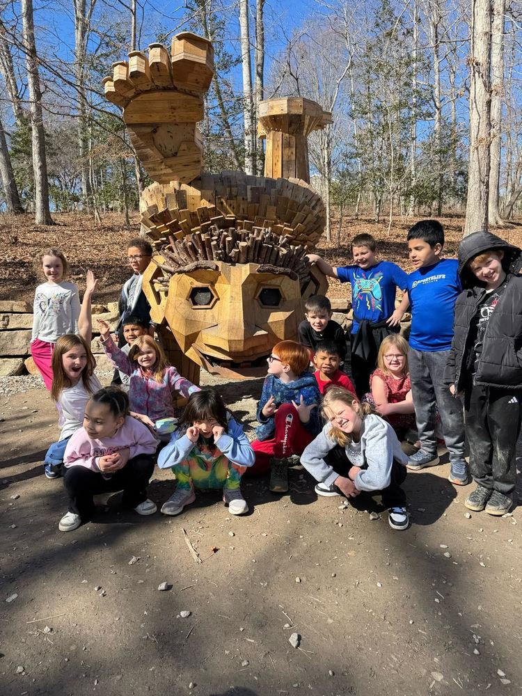 Students posing in front of a large wooden troll for a group photo.
