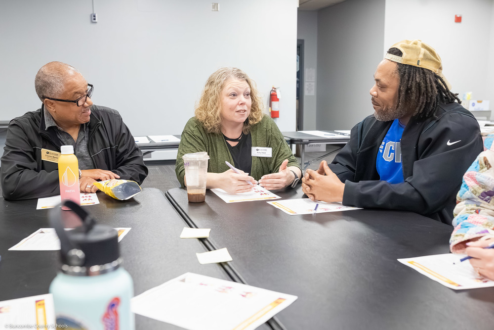 A school board member, principal, and parent sit at table having a discussion.