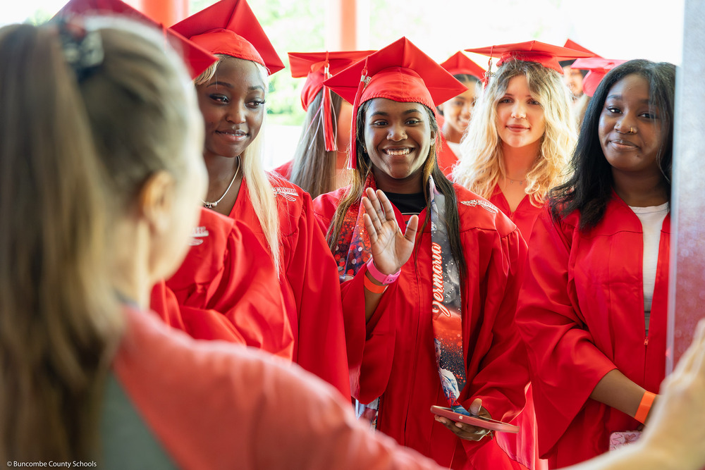 A group of Erwin seniors dressed in caps and gowns walks down a hallway