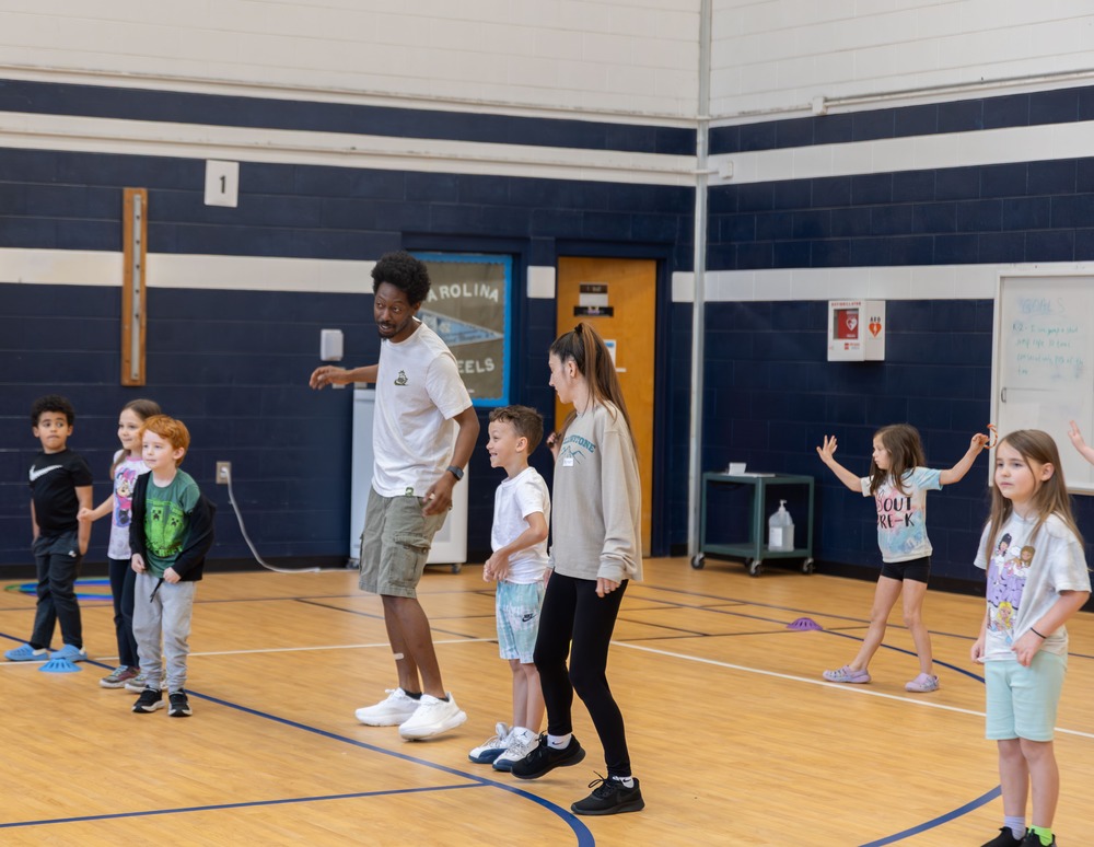 Students and two adults line dancing on gym floor 