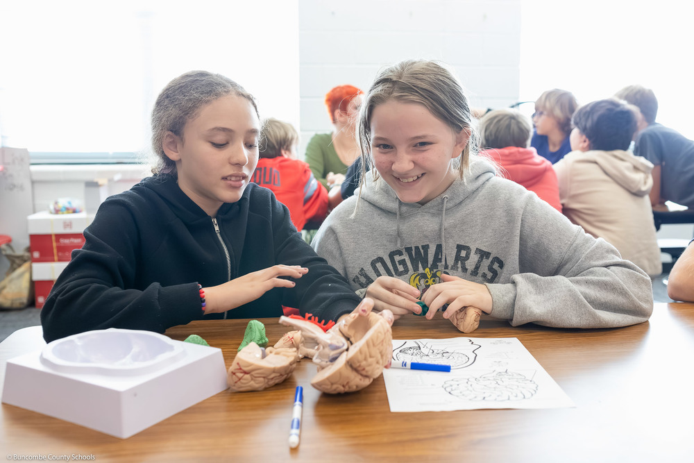 Two students smile at a brain model.