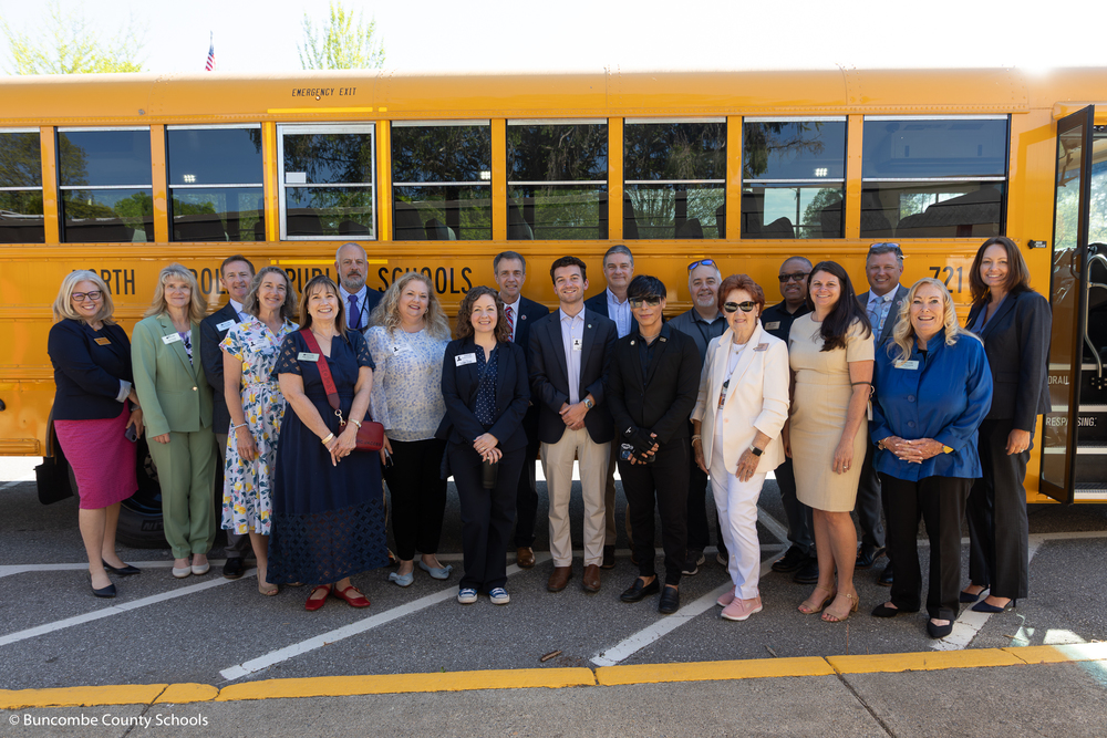 A photo of legislator guests posing in front of a school bus with BCS school leaders