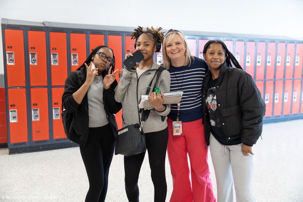 Ms. Hill stands with 3 students in front of a row of lockers and poses for a photo