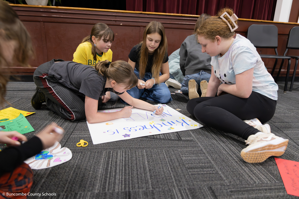 Four students sitting in the floor working on their kindness poster.