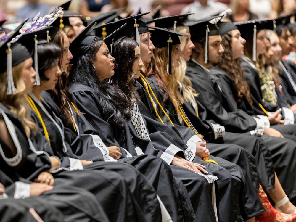 Members of the North Buncombe High School  Class of 2025 sit  in rows dressed in their caps and gowns .