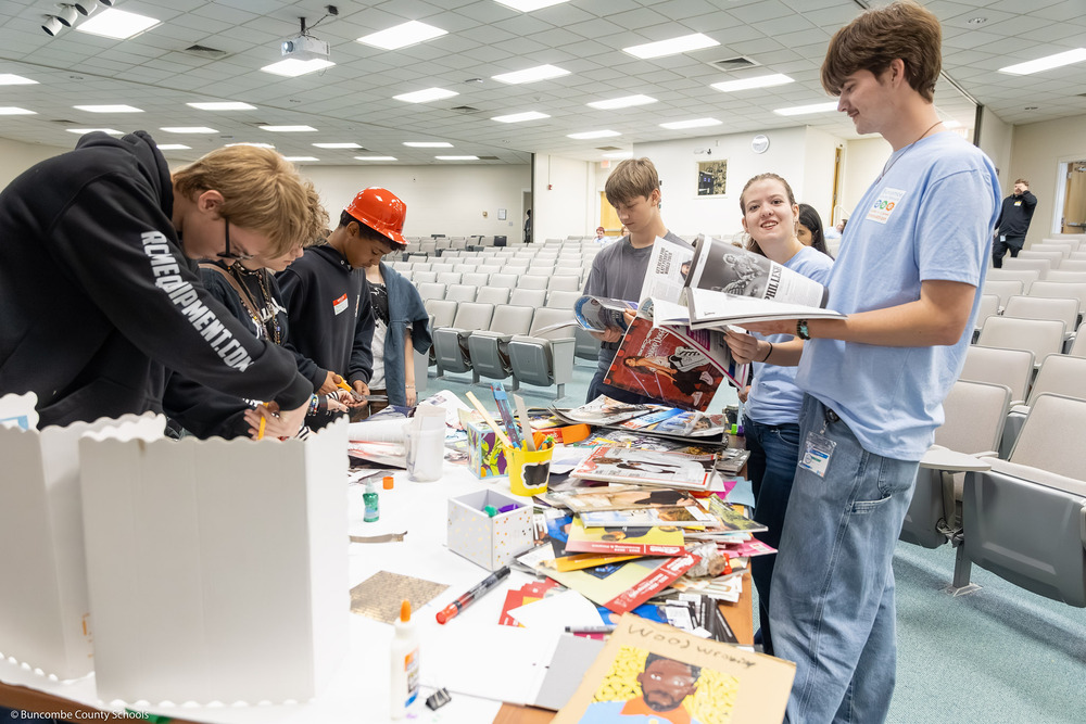 Six students stand around a table making collages.