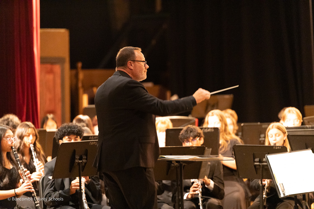 A band leader points his baton at student musicians playing on stage