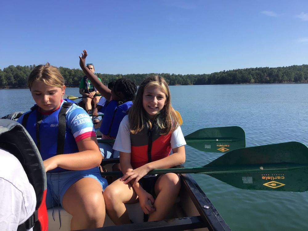 Students sitting in a canoe holding paddles on Lake James. 