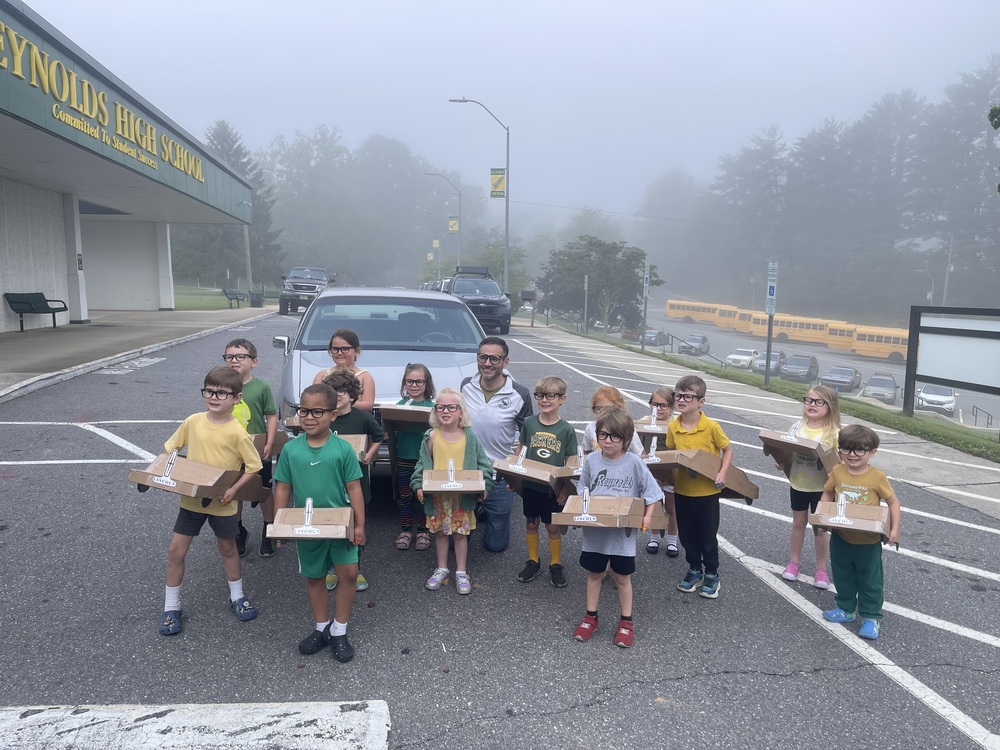 Principal Ben Alexander poses in front of his real car with Learning Lab students wearing model cars made of cardboard in the Reynolds High School parking lot.