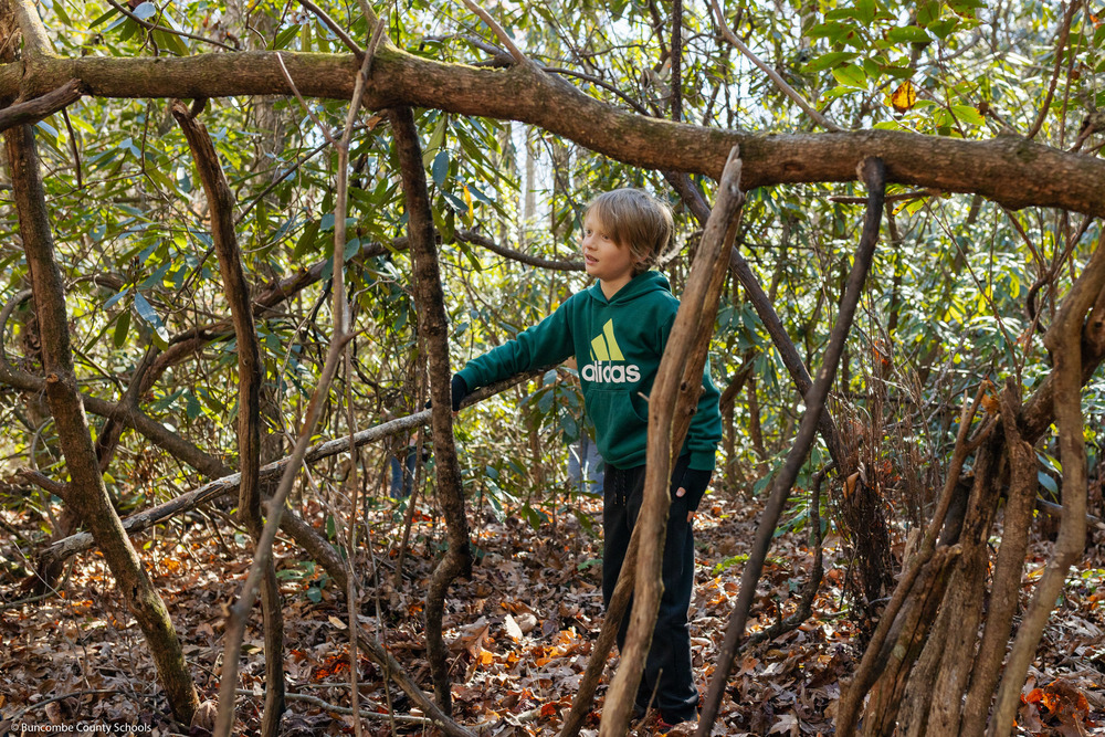 A student works on a shelter in the woods.