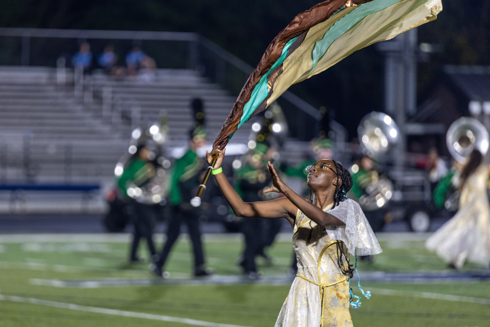 A member of the color guard catches her flag as tubas play in a line behind her.