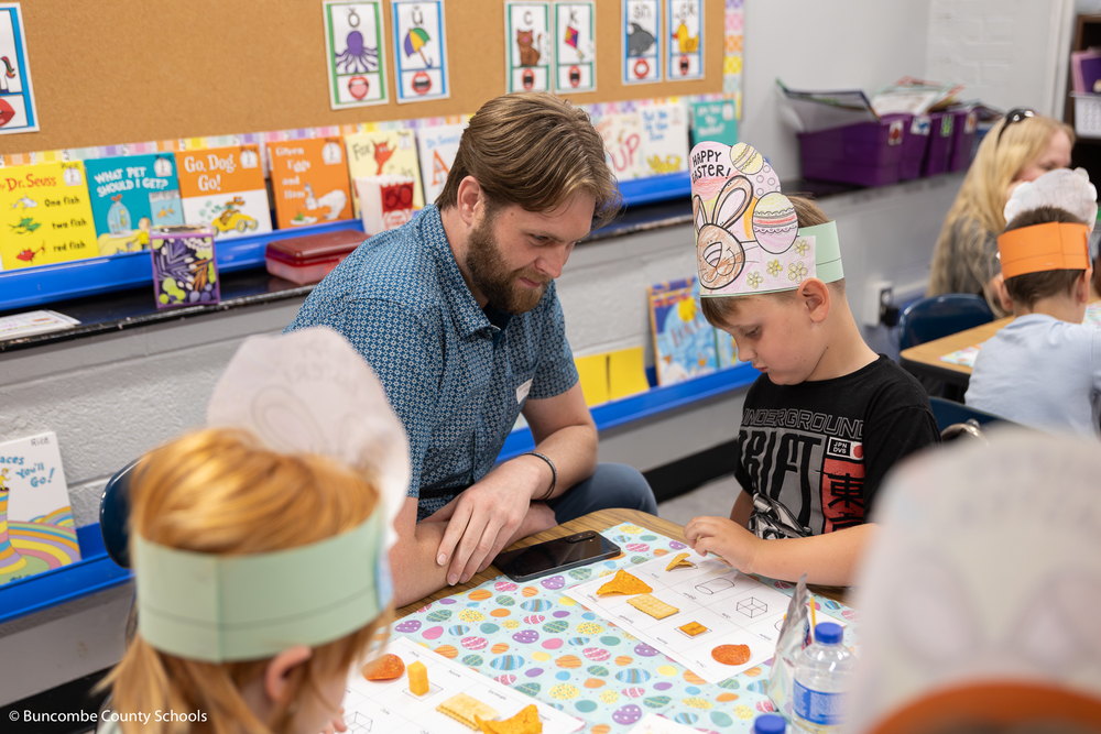 Student placing different food on a placemat. Student is matching the shapes on the placemat to the food. His dad is sitting beside him. 