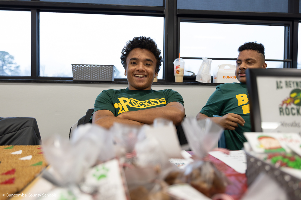 Male student with arms folded wearing a green shirt that says Rockets across the front smiling at the camera. 