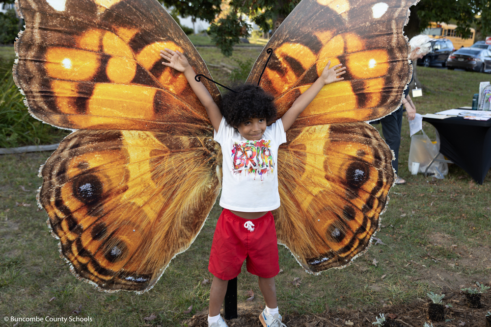 Boy standing in front of the butterfly wings for a photo. 