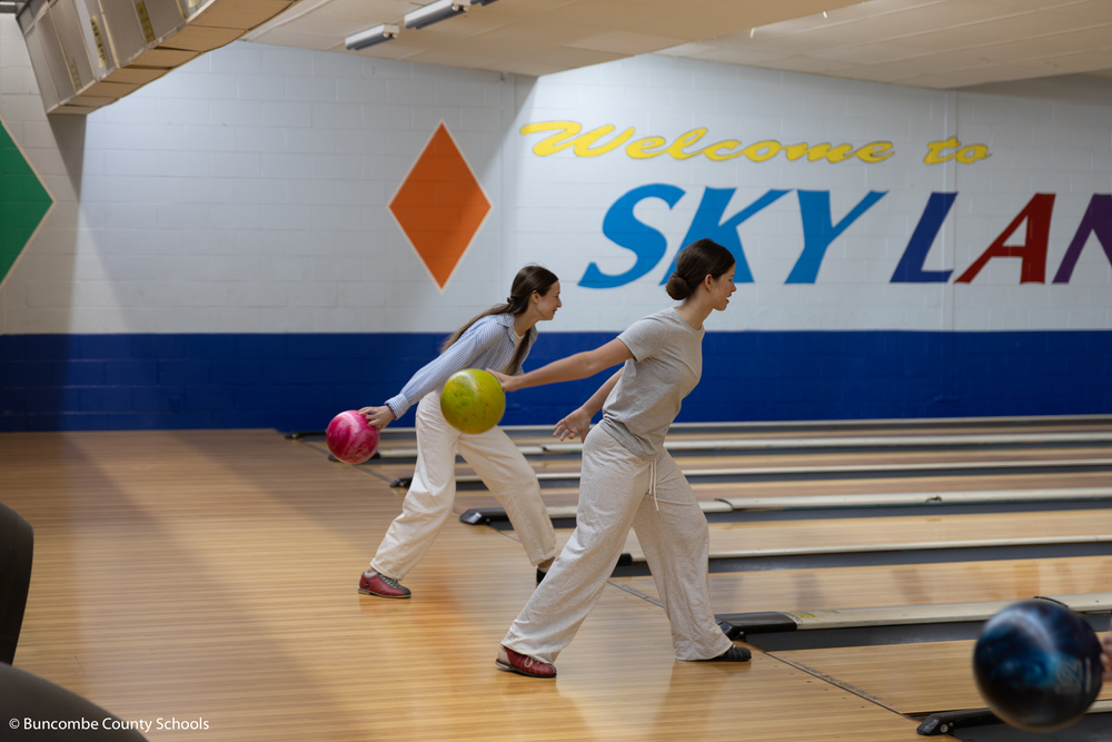 Two student rolling a bowling ball. 