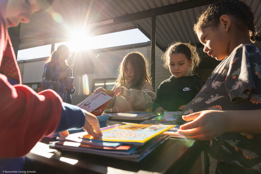 A student picks up a book from a table.