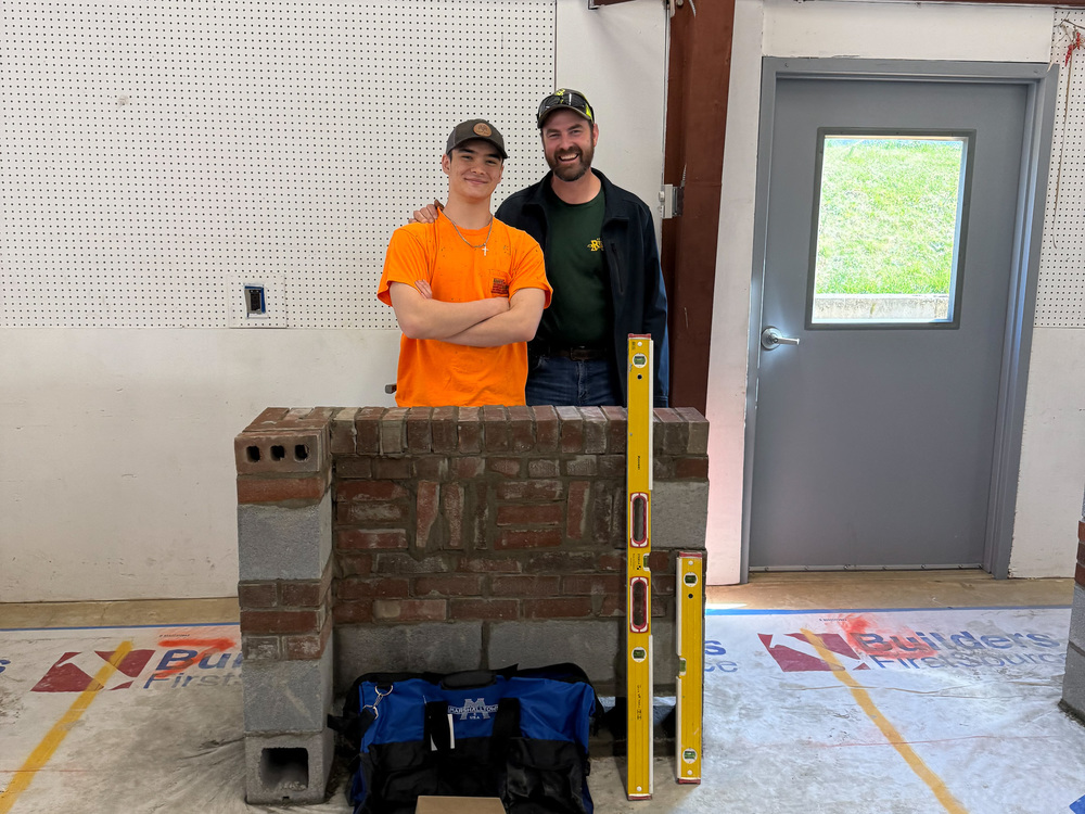 Gabriel stands next to Mr. Davis behind a wall he built in the competition.