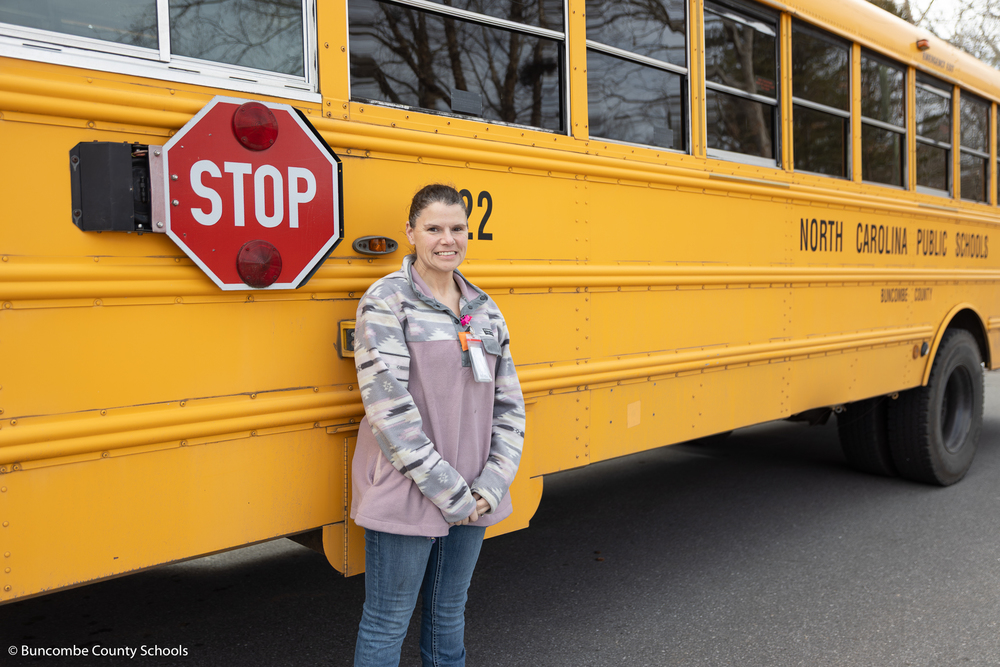 Lisa Rice standing in front of a yellow school bus smiling at the camera. 