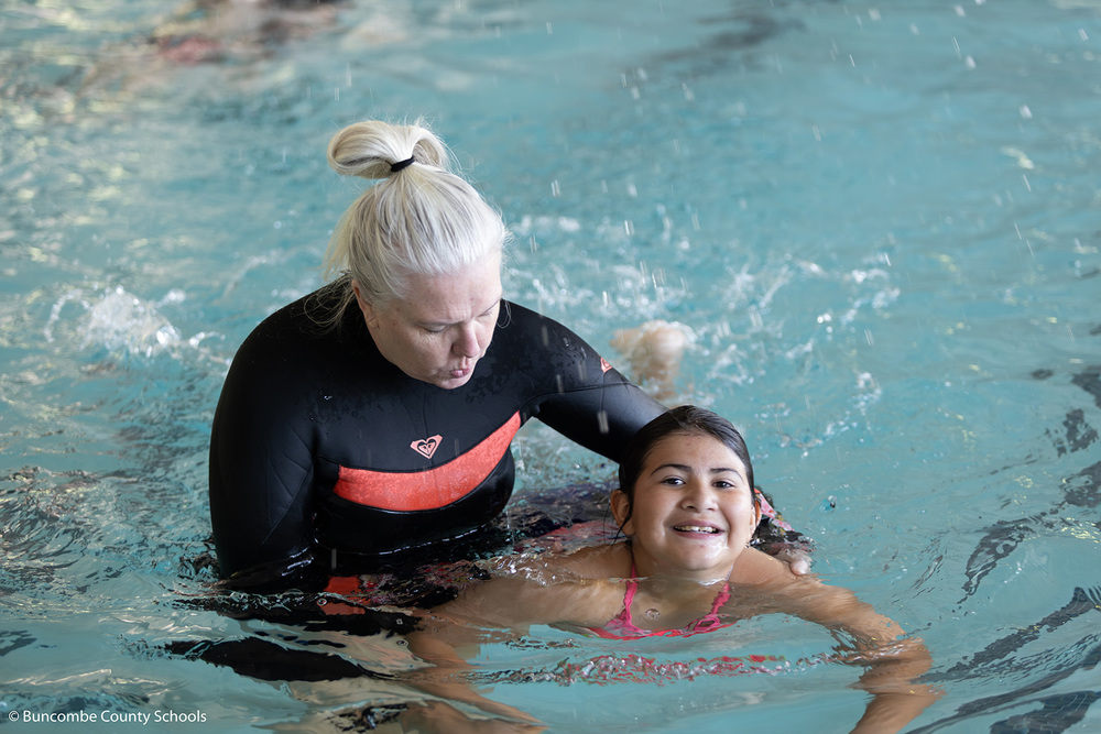 Young girl swimming in the pool with an instructor helping her.