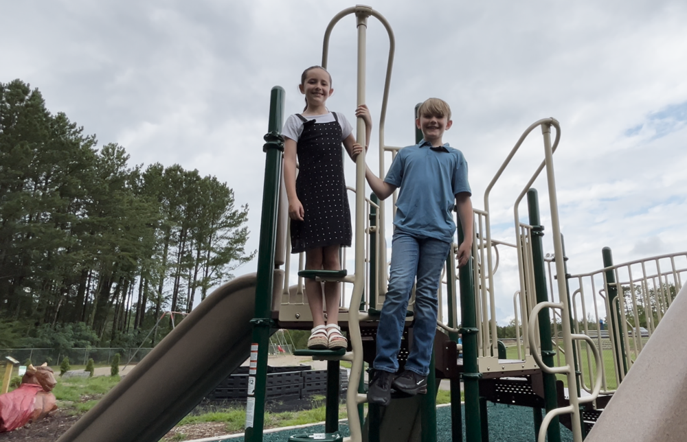 Two children at the top of the slide on a playground.