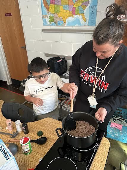 Student and teacher stirring a pot of browned ground beef as they make chili.