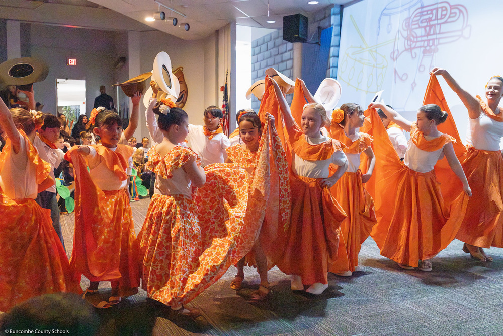 Students dance in a line of colorful orange and white outfits.