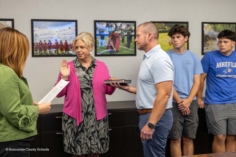 Dr. Reed holds up one hand and places the other on a Bible held by her husband as her two sons watch.
