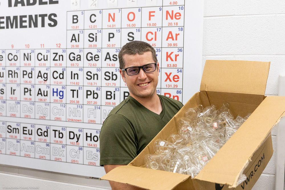 A BCS science teacher holds a box full of lab glass.