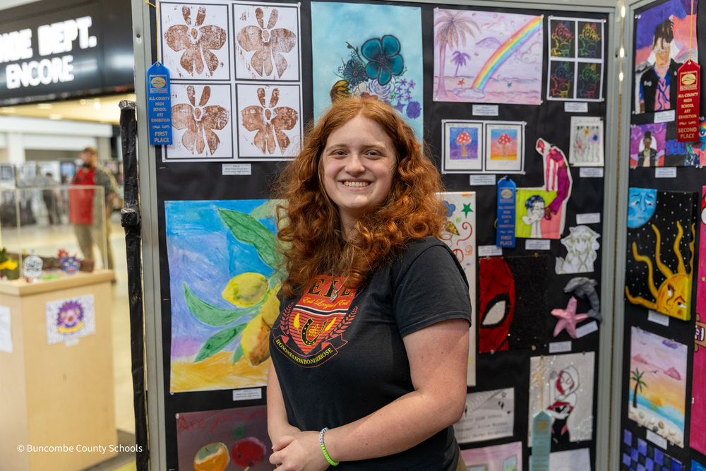 A student poses in front of her artwork on a divider in  Asheville Mall.