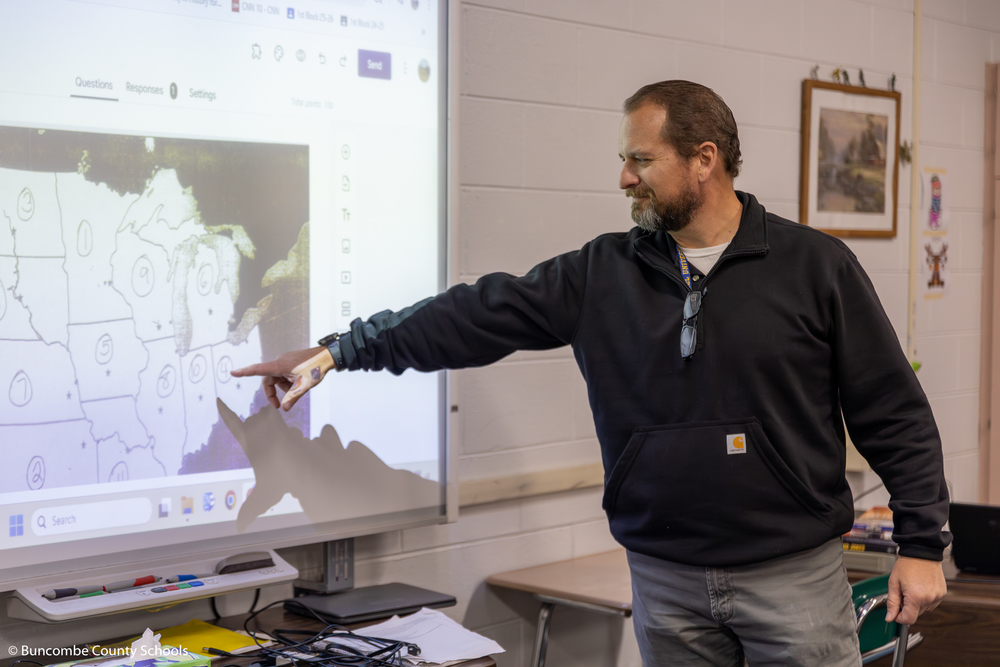 Mr. Gouge pointing at a dot on a map of the United States as students learn the states and their capitols. 