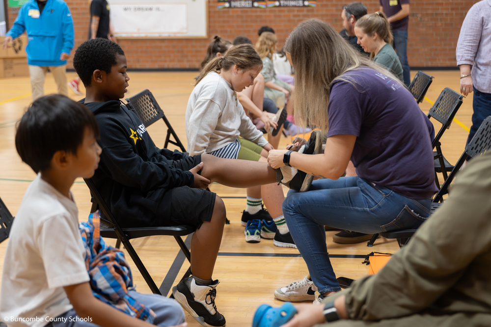 Male student trying on a new pair of shoes with the assistance of a volunteer.