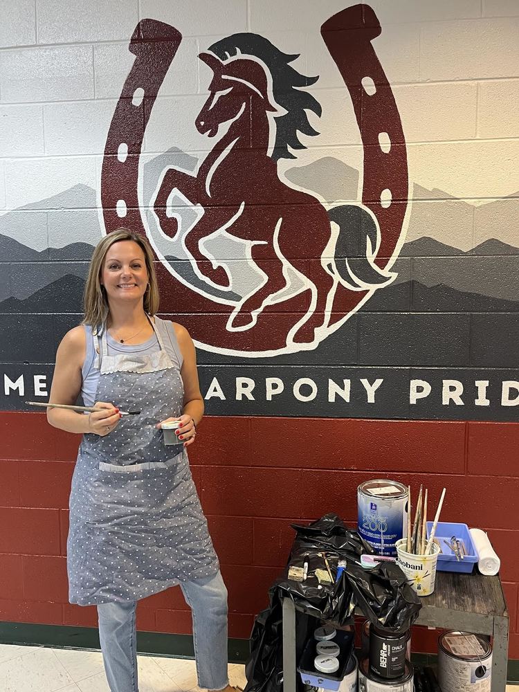 Mrs. Jolie Adtkins standing proudly in front of the warpony mural she painted at Black Mountain Elementary.