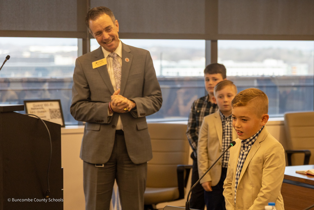 Dr. Jackson stands near a West Buncombe student speaking into a microsphone at the state board of education meeting.