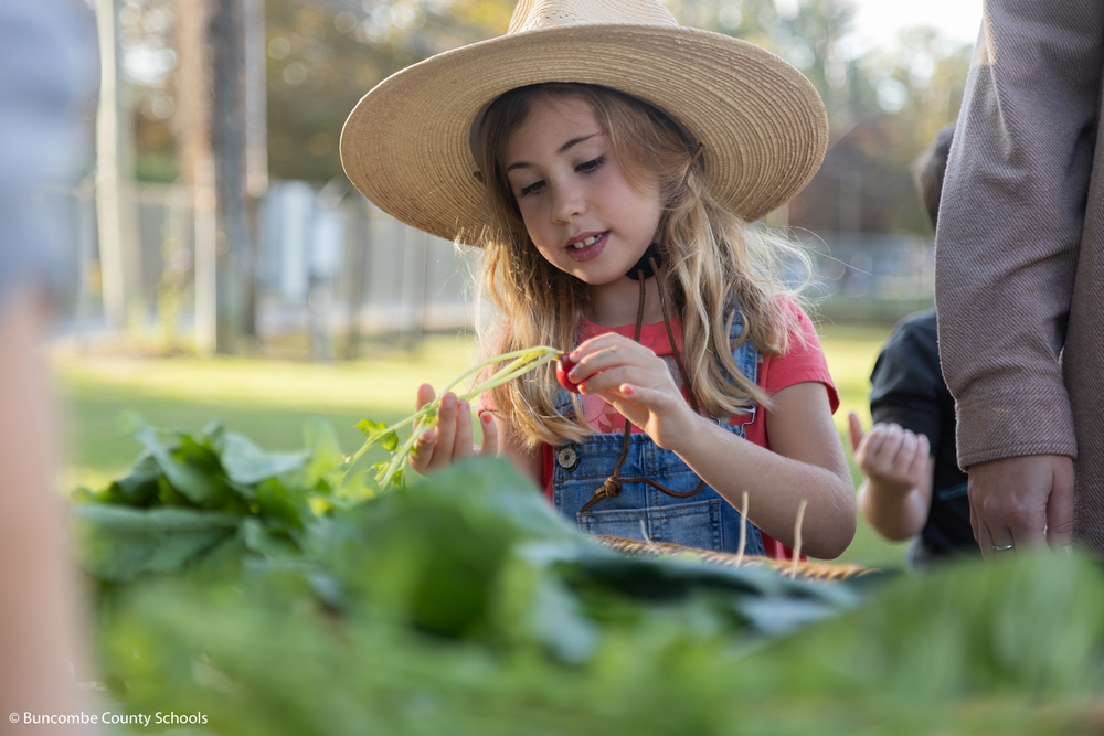 Little girl dressed up like a farm holding a radish.