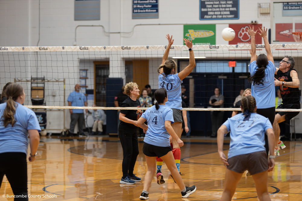 Hominy Valley volleyball team jumping in the air to block the volleyball being hit by Candler Elementary.