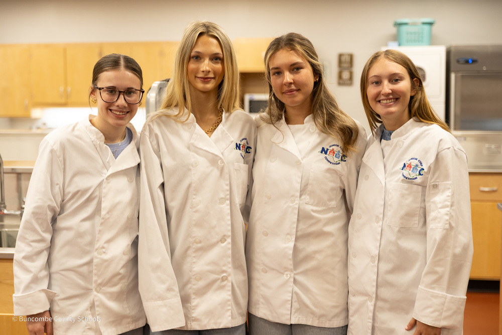 The 4 members of the Tastebud Trailblazers pose in the classroom kitchen wearing their chef's jackets