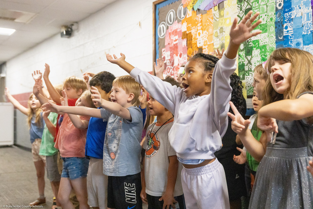 Students raise their hands while singing "The Dot Song."