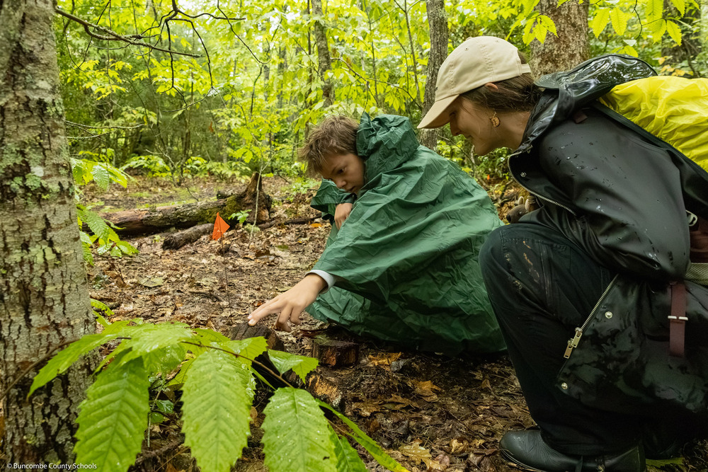 A student flips a log while a ranger looks on.