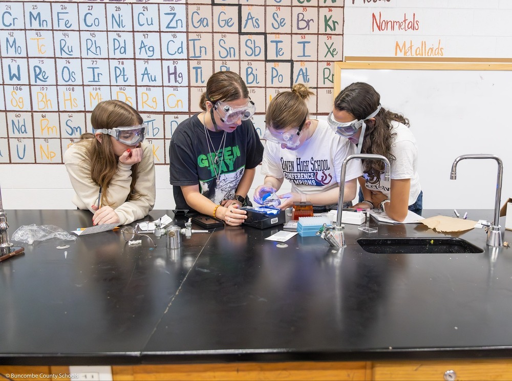 Four students, wearing safety goggles, work on a DNA test.