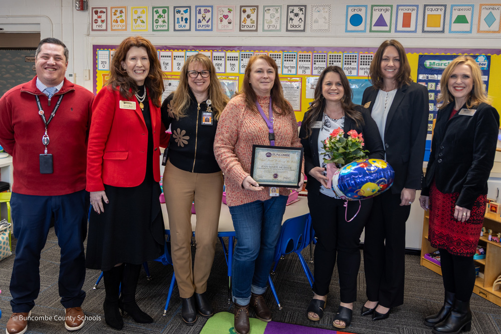 Mrs. McBride poses for a photo in a classroom holding a certificate. She has three people on both sides of her: the Student Services team and the principals for the three schools she serves.
