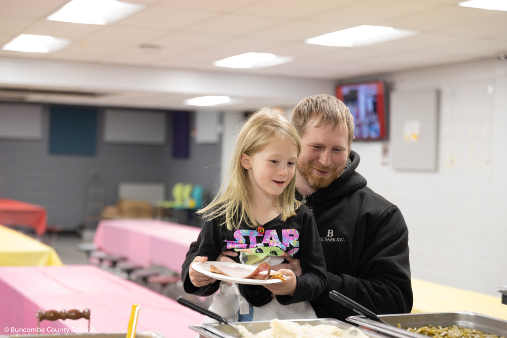 Father holding his young daughter up so she can see the food in the buffet line.