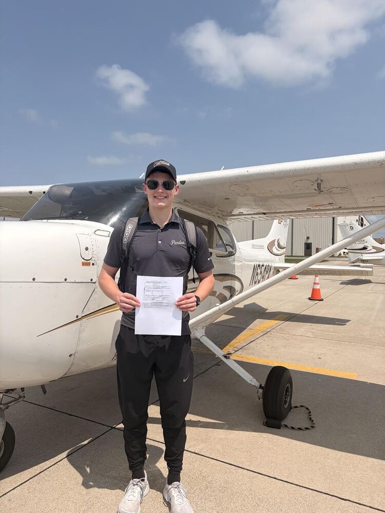 Carter Starke holding a piece of paper in front of a small airplane. 