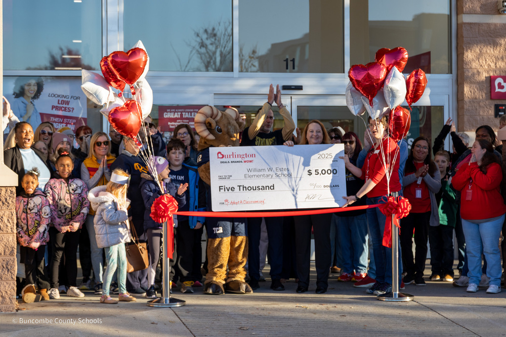 Estes teachers, students, and parents stand in front of Burlington in front of a red ribbon. There is a giant novelty check for $5,000 to the school from Burlington.