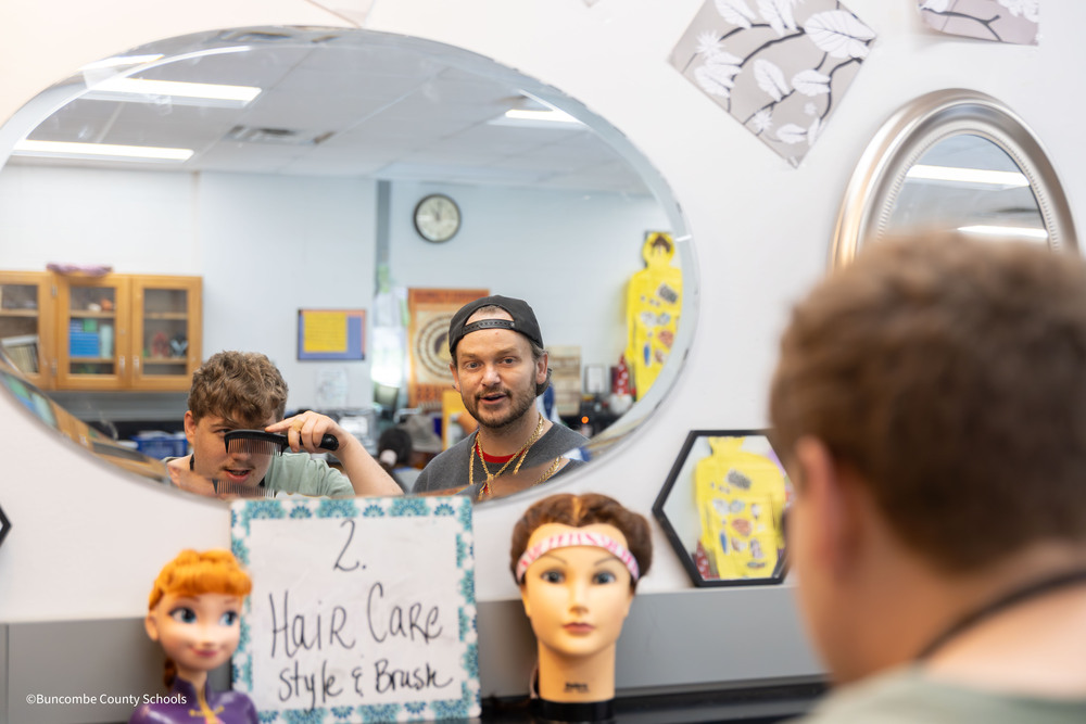 Student looks in mirror and combs hair while Tyler Plemmons watches