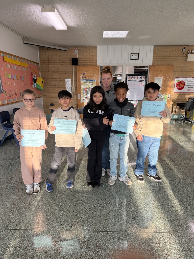 Five fourth grade students stand in front of their teacher holding their perfect attendance certificates. 