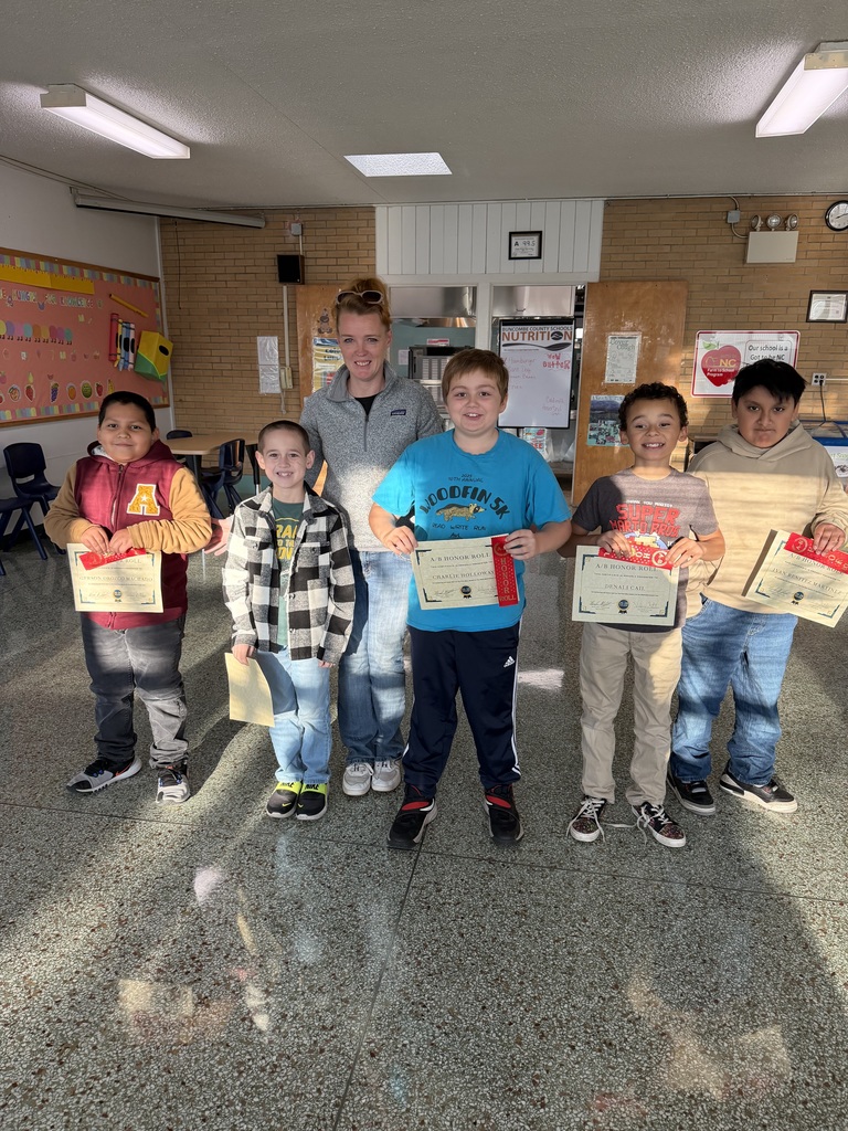 Five fourth grade students stand in front of their teacher holding their A/B honor roll certificates. 