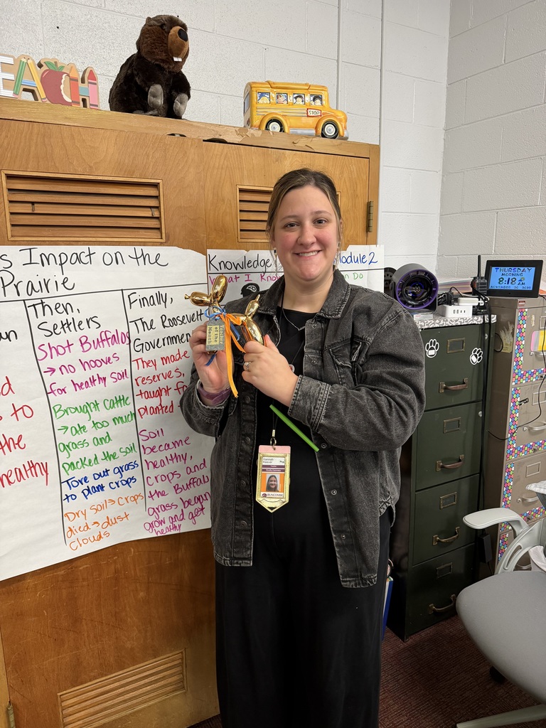 Teacher standing in front of wall holding a shiny puppy statue.