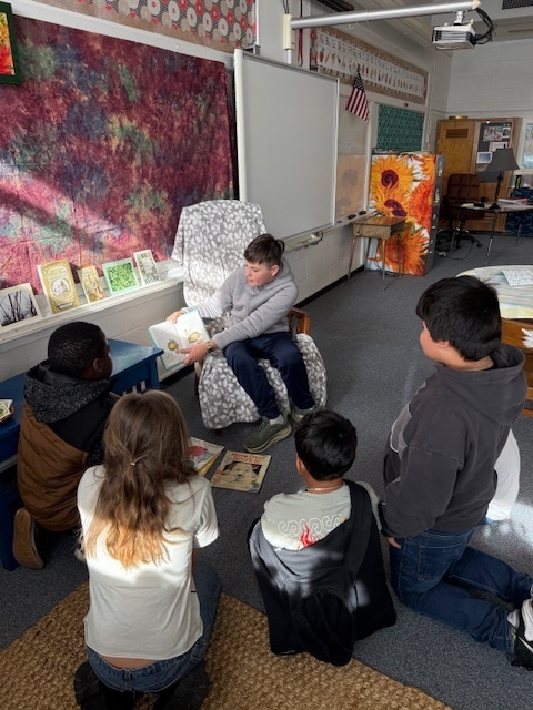 Middle school student reads to four fourth grade students. 