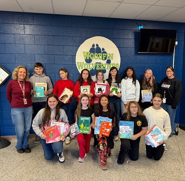 Students stand in front of Woodfin Wolverine sign holding up books.